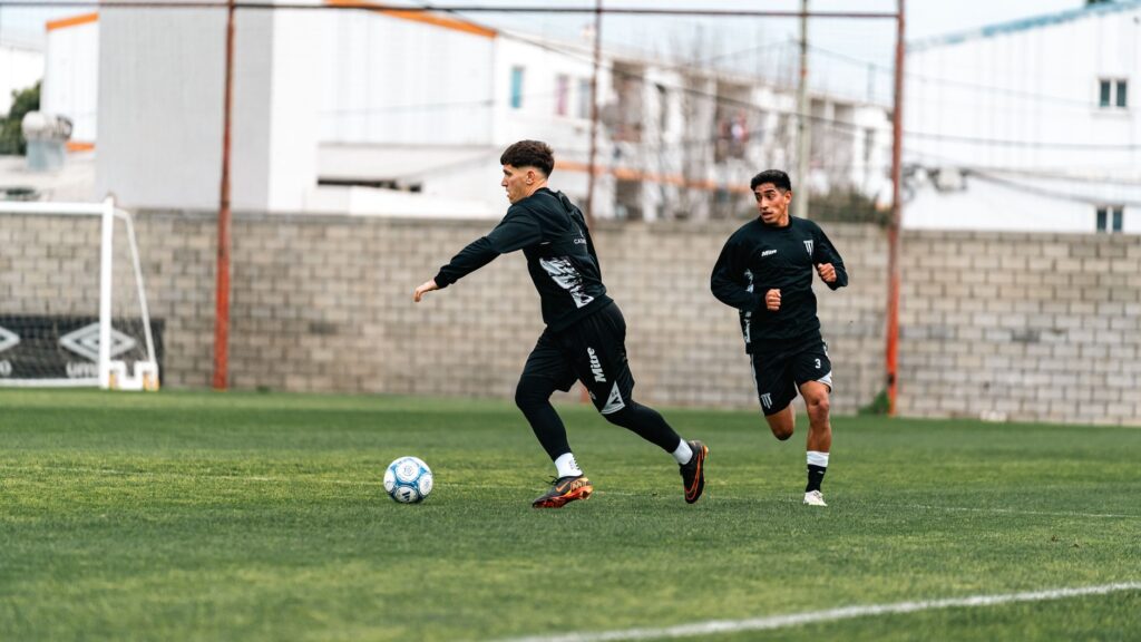Two soccer players training intensely on a green field during daytime.