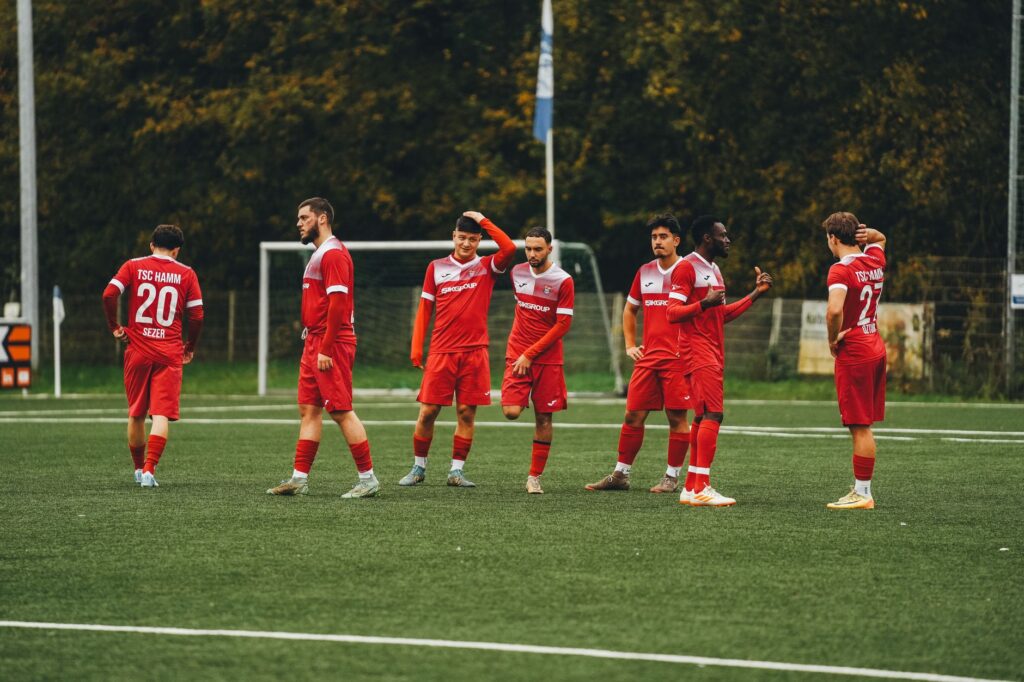 Amateur soccer team in red uniforms gathering on a green field during daytime.