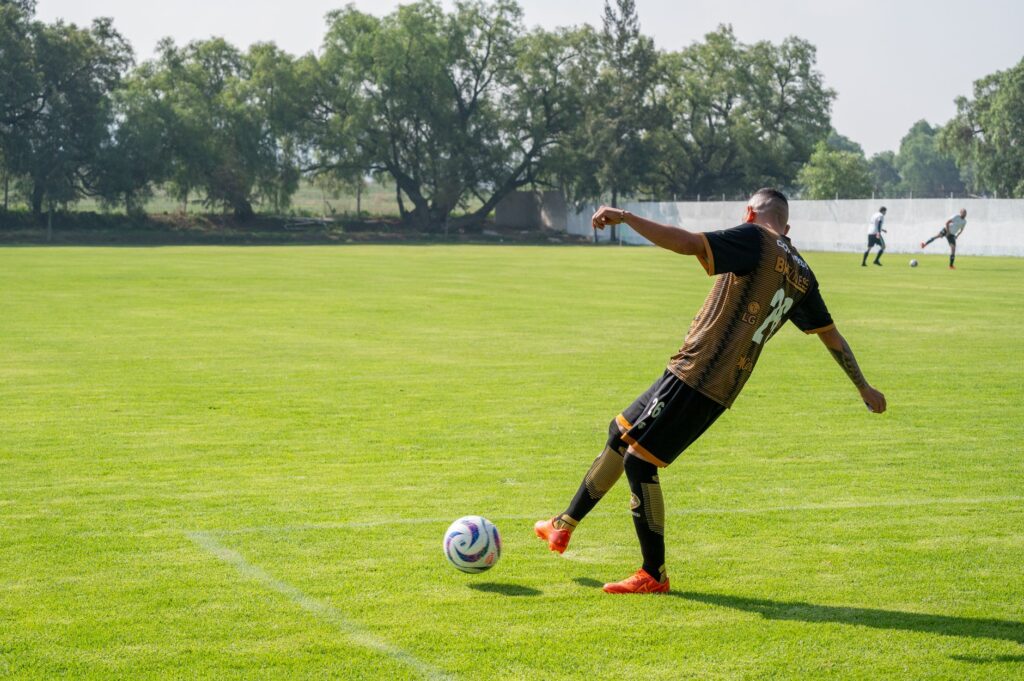 Adult male soccer player kicking a ball during training on a sunny day.