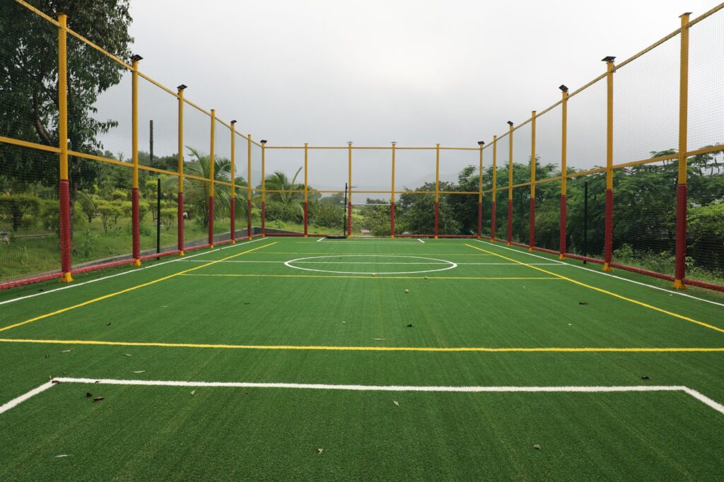 Vibrant outdoor futsal court with artificial turf surrounded by a net in a lush setting.