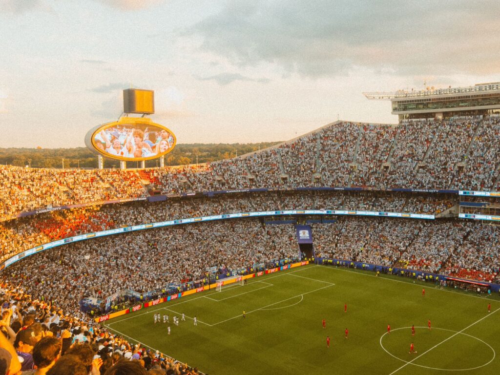 Aerial view of a packed soccer stadium during a lively match at sunset.